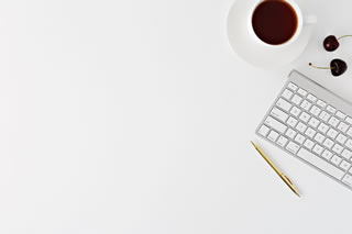 A white desk with a coffee, two cherries, a keyboard and a pen