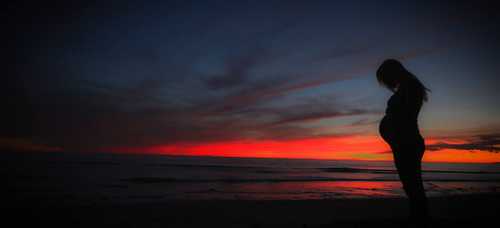 Woman on beach at sunset who is pregnant