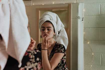 A girl with a towel on her hair looking in the mirror