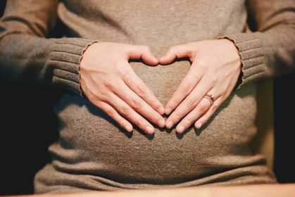 A woman making a heart shape with her hands on her pregnancy belly